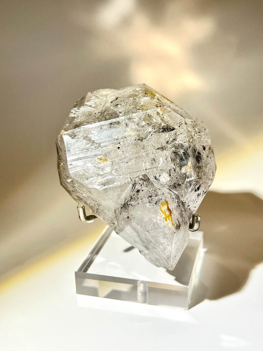 一顆透明的 閃靈鑽 Herkimer Diamond，在暖光下呈現自然層紋與清晰雙尖結構。