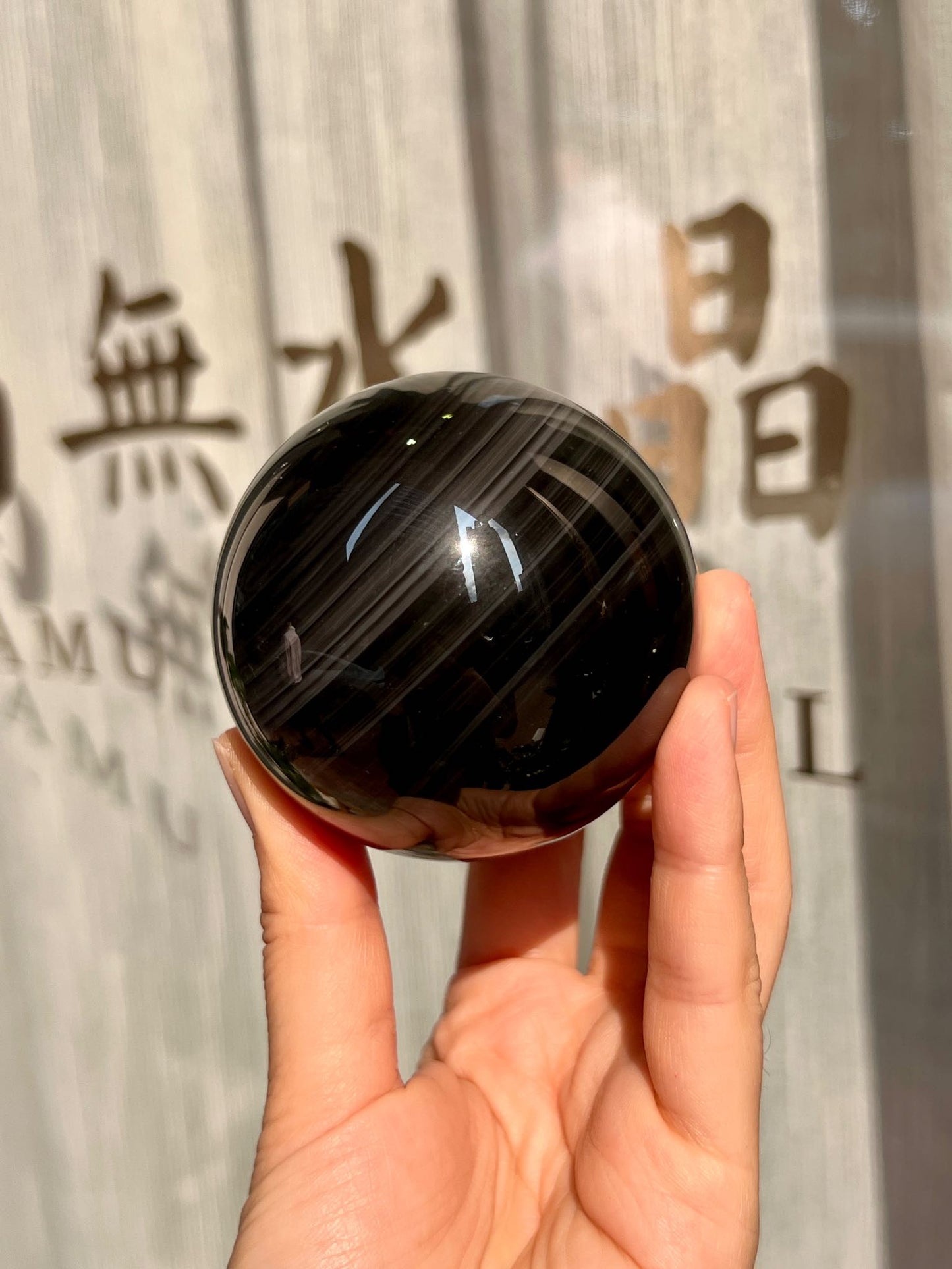 大款黑曜石水晶球在陽光下呈現深色柔光與層圈