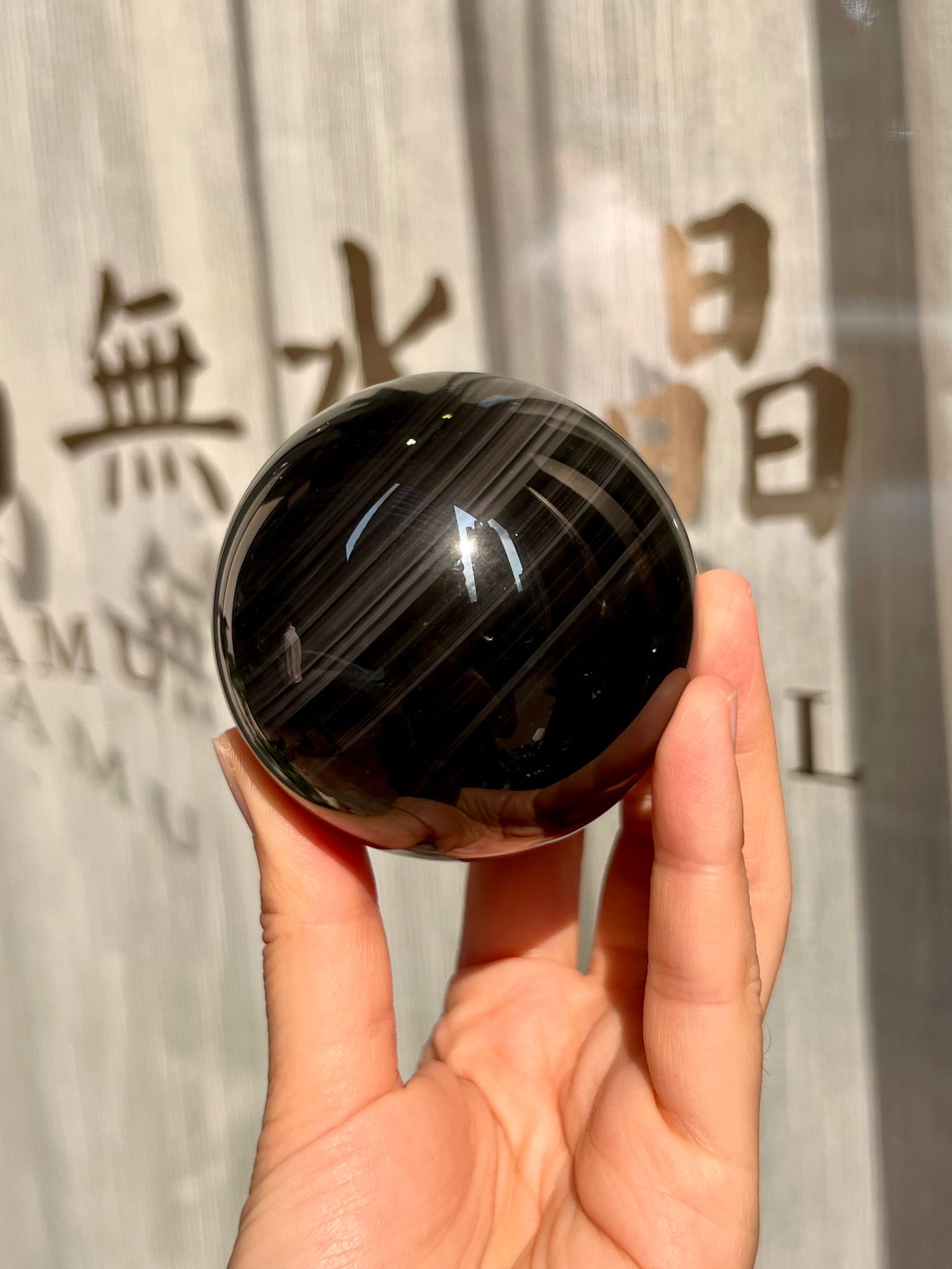 大款黑曜石水晶球在陽光下呈現深色柔光與層圈